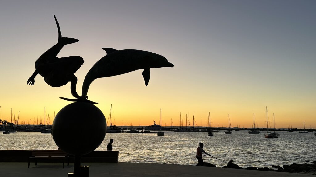 Dolphin sculpture silhouetted against a waterfront sunset